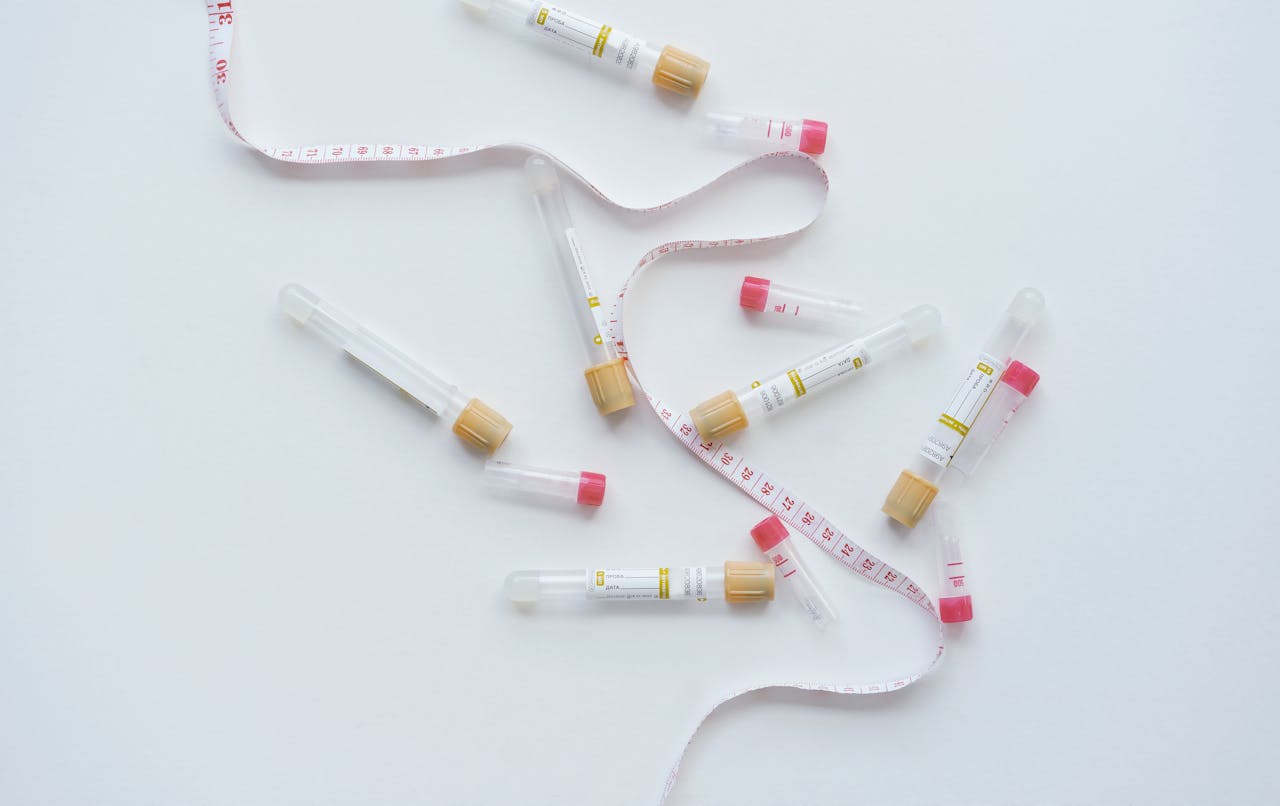 Flat lay of blood test tubes and a tape measure on a white background.